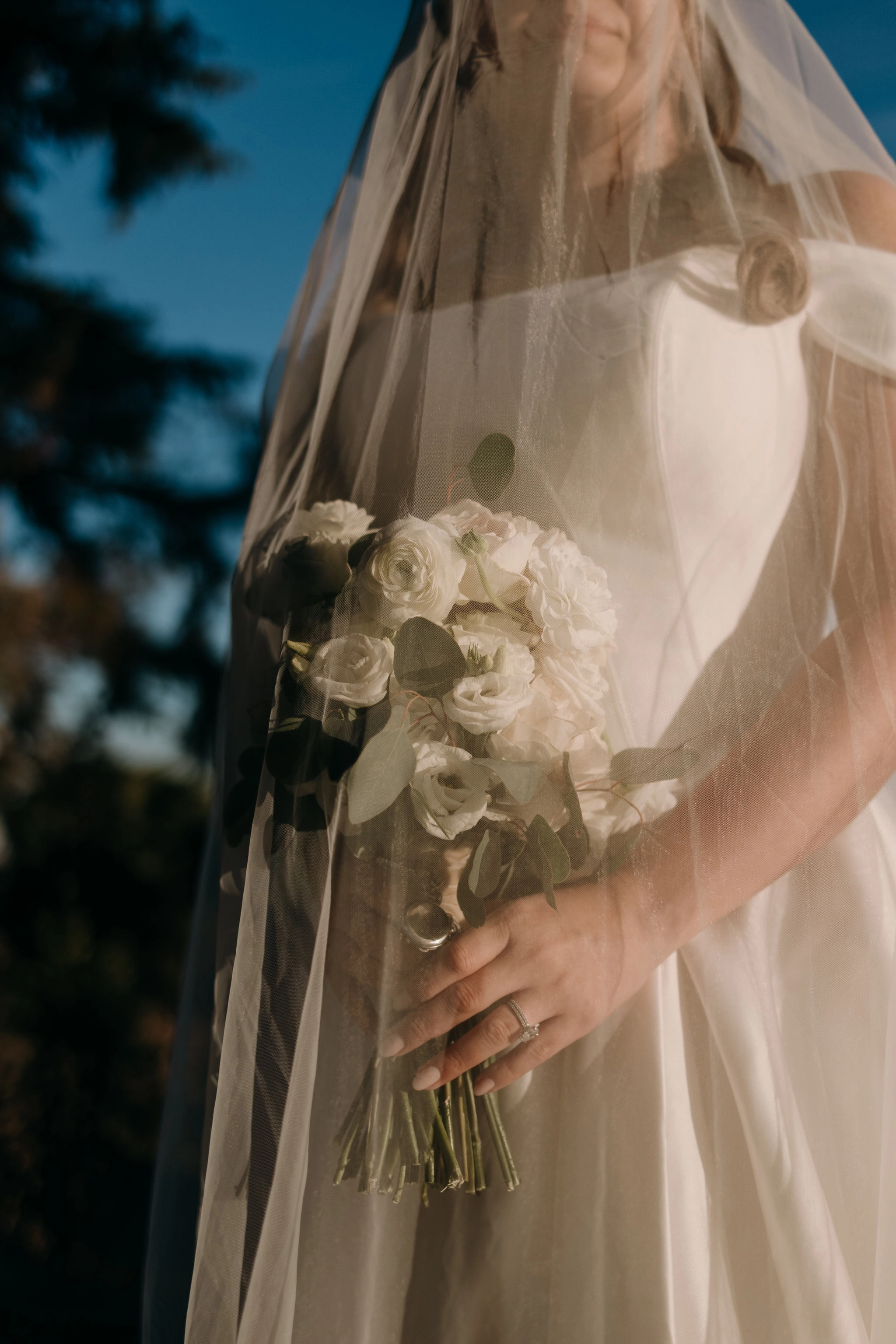 Novia, cuya presencia se suaviza tras el delicado velo, con un ramo que destaca por su elegancia clásica y natural con flores blancas.